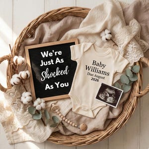 May include: A neutral-toned baby announcement scene in a woven basket. Includes a letter board with the text "We're Just As Shocked As You", a onesie with the text "Baby Williams Due August 2026", and a sonogram image.