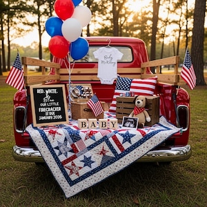May include: A red vintage truck bed is decorated with patriotic items for a baby announcement. It includes a quilt, balloons, flags, a letter board that reads "Red, White, Blue, Our Little Firecracker is Due January 2026", and a baby onesie.
