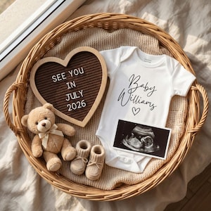 Może przedstawiać: Wiklinowy kosz zawiera tablicę w kształcie serca z napisem "SEE YOU IN JULY 2026", białe body z napisem "Baby Williams", pluszowego misia, buciki dla dziecka i obraz USG. Przedmioty ułożone są na beżowym kocu.