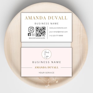 Puede incluir: Dos tarjetas de visita. La tarjeta superior es blanca con texto dorado, incluyendo el nombre "AMANDA DUVALL" e información de contacto. La tarjeta inferior es rosa, con un logotipo y el nombre "AMANDA DUVALL" en dorado. Para uso comercial.