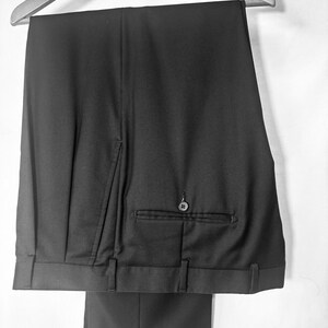 May include: Black dress pants hanging on a wooden hanger. The pants have a buttoned back pocket and belt loops. The bottom of the pants are cuffed.