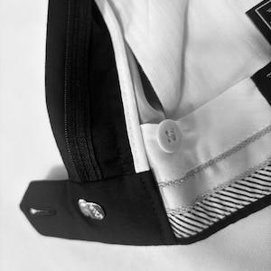 May include: Close-up of a black and white suit pant. The image shows the button closure, zipper, and interior lining. The white lining has a subtle striped pattern. The black fabric is smooth and tailored.