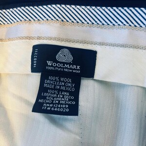May include: Close-up of a garment label with the Woolmark logo, indicating 100% pure new wool. The label also states the item is dry clean only and made in Mexico. The background shows the fabric's texture.