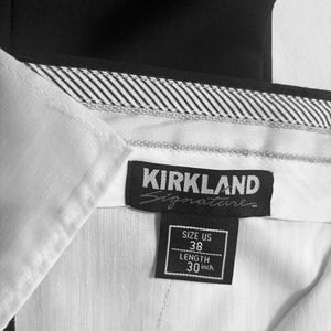 May include: Close-up of a black and white label from Kirkland Signature pants. The label indicates a US size 38 with a 30-inch length. The pants are black with a white interior and a striped waistband.