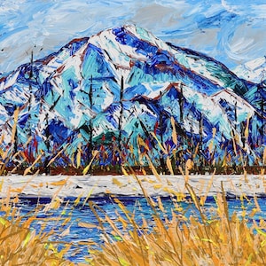 May include: An original oil painting of a mountain landscape. The artwork depicts snow-capped mountains in shades of blue and white, with a foreground of golden grasses and a blue river. The sky is a light blue with brushstrokes.