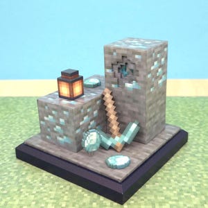 May include: A miniature Minecraft-themed diorama featuring pixelated blocks, a pickaxe, and diamond ore. A small lantern with a glowing orange light sits atop a block. The base is dark purple, and the background is a light blue.