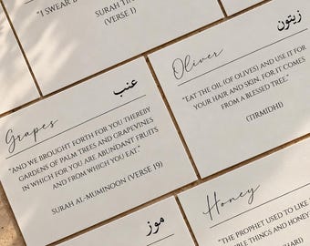 May include: A set of five white rectangular cards featuring black printed text in English and Arabic. Each card displays a food name, a corresponding religious quote, and a source citation. The cards are arranged on a light-coloured surface.
