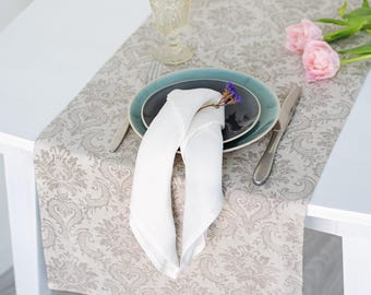 Könnte beinhalten: Tischarrangement mit beigem Damast-Tischläufer, türkisfarbenem Teller, weißer gefalteter Serviette und klarem Glas. Rosa Tulpen und ein silbernes Messer vervollständigen die elegante Anordnung.