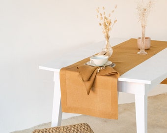 Könnte beinhalten: Ein weißer Tisch mit einem braunen Tischläufer aus Leinen und einer weißen Tasse mit Untertasse. Ein geflochtener Hocker aus Weide steht vor dem Tisch. Getrocknete Blumen stehen in Vasen auf dem Tisch.