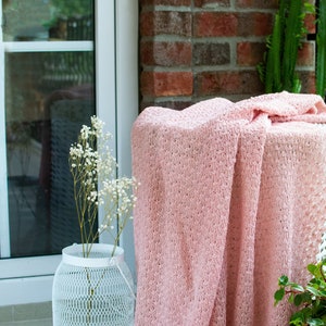 K&ouml;nnte beinhalten: Eine rosafarbene H&auml;keldecke, die &uuml;ber eine wei&szlig;e Metall-Laterne mit einem Strau&szlig; wei&szlig;er Baby's Breath-Blumen gelegt wird. Die Decke hat ein zartes, offenes Muster.