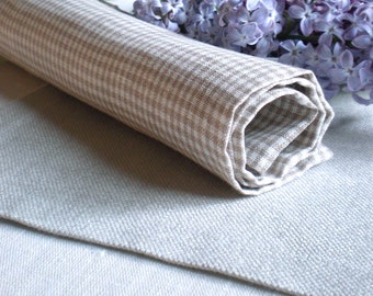 May include: A rolled up beige and white checkered linen kitchen towel on a white linen tablecloth with a bouquet of purple lilac flowers.