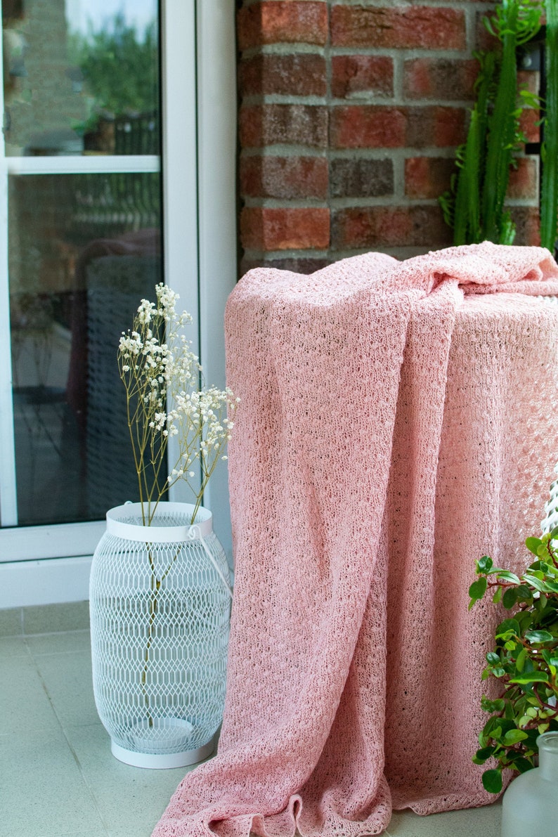 K&ouml;nnte beinhalten: Eine rosafarbene H&auml;keldecke, die &uuml;ber eine wei&szlig;e Metall-Laterne mit einem Strau&szlig; wei&szlig;er Baby's Breath-Blumen gelegt wird. Die Decke hat ein zartes, offenes Muster.