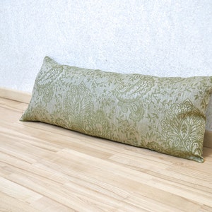 Könnte beinhalten: Ein langes, grünes, gemustertes Kissen mit Paisley-Muster. Das Kissen liegt auf einem hellen Holzboden.