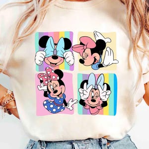 Może przedstawiać: Kremowy t-shirt z kolorową grafiką Myszki Minnie w czterech r&oacute;żnych pozach. Każda Myszka Minnie jest umieszczona na pastelowym tle. Projekt zawiera kokardy i grochy.