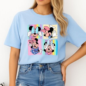 Może przedstawiać: Jasnoniebieska koszulka z grafiką Myszki Minnie w czterech r&oacute;żnych pozach. Każda poza jest umieszczona w kwadracie z pastelowym tęczowym tłem. Koszulka jest w stylu casual, z kr&oacute;tkim rękawem.