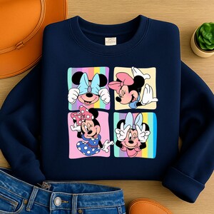 Może przedstawiać: Granatowa bluza z kolorową grafiką Myszki Minnie w czterech r&oacute;żnych pozach. Każda poza umieszczona jest w kwadracie z pastelowym tęczowym tłem. Bluza wykonana jest z miękkiego materiału.