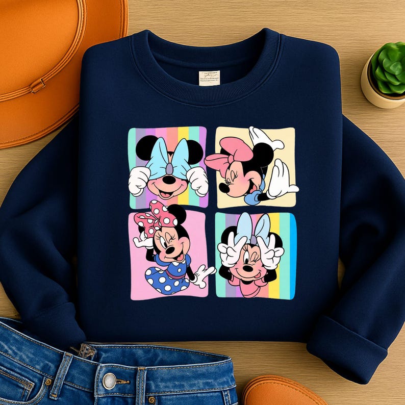 Może przedstawiać: Granatowa bluza z kolorową grafiką Myszki Minnie w czterech r&oacute;żnych pozach. Każda poza umieszczona jest w kwadracie z pastelowym tęczowym tłem. Bluza wykonana jest z miękkiego materiału.