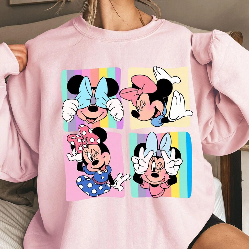 Może przedstawiać: Jasnor&oacute;żowa bluza z kolorową grafiką Myszki Minnie w czterech r&oacute;żnych pozach. Każdy kwadrat ma inny kolor tła, a Myszka Minnie ma na sobie kokardę. Bluza wykonana jest z miękkiego materiału.