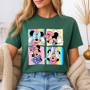 Może przedstawiać: Zielona koszulka z kolorową grafiką Myszki Minnie w czterech r&oacute;żnych pozach. Każda poza jest umieszczona w kwadracie z pastelowym tęczowym tłem. Myszka Minnie nosi kokardy i sukienki w r&oacute;żnych kolorach.