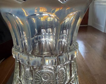 May include: A clear glass vase with an opalescent finish, featuring a scalloped rim and a textured body. The design includes a horizontal band of rectangular panels above a section with circular starburst patterns and a diamond-cut base.