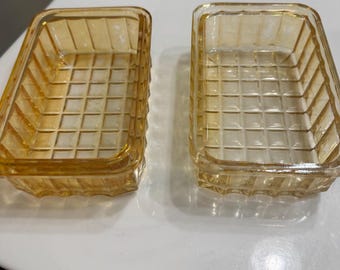 May include: Two rectangular, amber-colored glass dishes. Each dish has a grid pattern on the bottom and sides. The dishes are empty and sit side-by-side on a white surface.