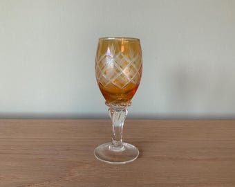 May include: An amber-colored, stemmed glass with a diamond-patterned design etched into the bowl. The glass has a clear, ornate stem and a round base. The glass is likely used for serving a beverage.
