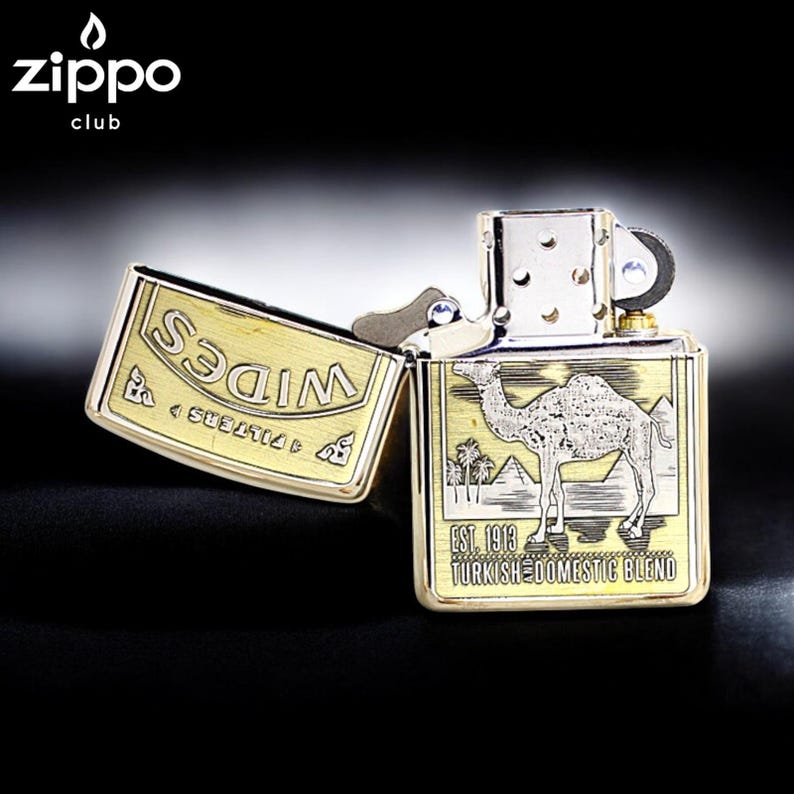 Pode incluir: Um isqueiro Zippo com acabamento dourado e prateado. O isqueiro apresenta um design de camelo e pir&acirc;mide com o texto "EST. 1913 TURKISH DOMESTIC BLEND". A tampa tem a palavra "WIDES" gravada.