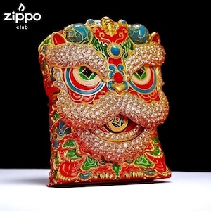 May include: A Zippo lighter featuring a detailed, ornate design of a lion's head. The lighter is primarily red, gold, and green, with accents of blue and white. The lion's face is encrusted with small, sparkling stones, and the design is highly detailed.