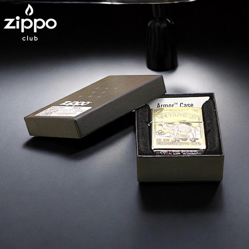 Pode incluir: Um isqueiro Zippo dourado com um design de camelo, apresentado numa caixa cinza escuro. O isqueiro est&aacute; rotulado como "Armor Case" e inclui o log&oacute;tipo Zippo. A caixa est&aacute; aberta, revelando o isqueiro no interior.