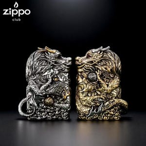May include: Two Zippo lighters with dragon designs. One is silver, the other gold. The lighters feature detailed dragon scales, claws, and heads. The Zippo club logo is in the upper left corner.