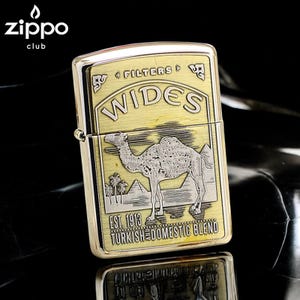 Pode incluir: Um isqueiro Zippo dourado com um design de camelo. O isqueiro apresenta a palavra "WIDES" e o texto "EST. 1913 TURKISH DOMESTIC BLEND". O logotipo do clube Zippo est&aacute; no canto superior esquerdo. O isqueiro est&aacute; sobre uma superf&iacute;cie reflexiva.