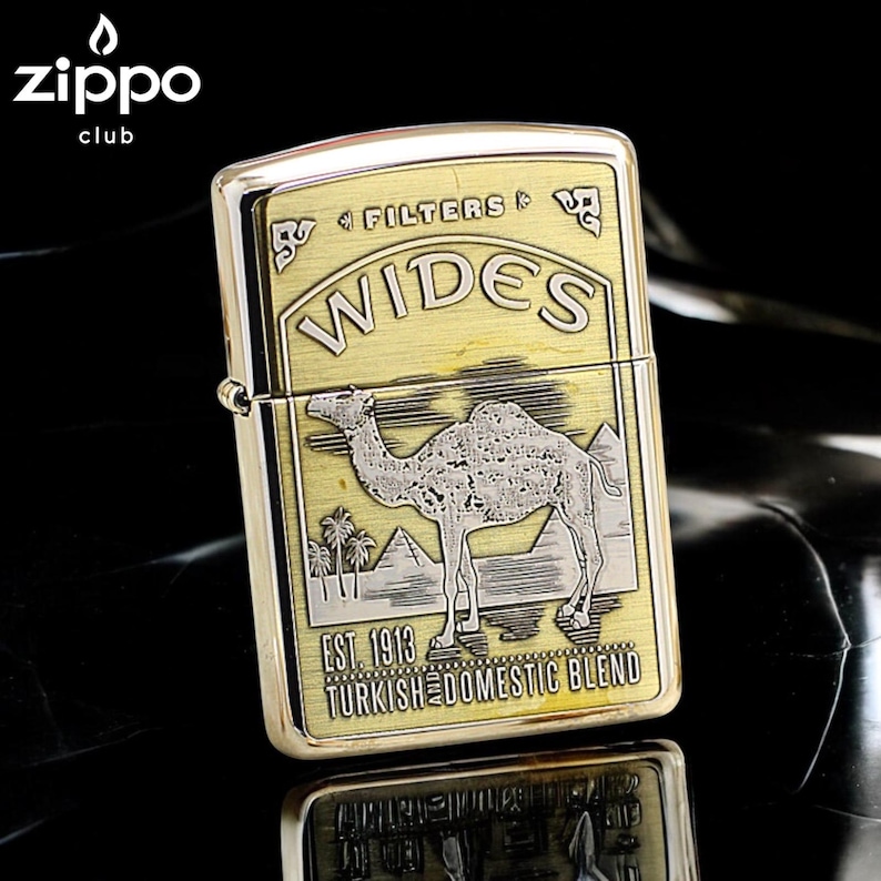 Pode incluir: Um isqueiro Zippo dourado com um design de camelo. O isqueiro apresenta a palavra "WIDES" e o texto "EST. 1913 TURKISH DOMESTIC BLEND". O logotipo do clube Zippo est&aacute; no canto superior esquerdo. O isqueiro est&aacute; sobre uma superf&iacute;cie reflexiva.