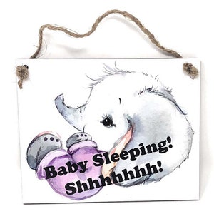 May include: A white wooden sign with a watercolor illustration of a baby elephant holding a pair of purple mittens. The sign reads "Baby Sleeping! Shhhhhhh!"