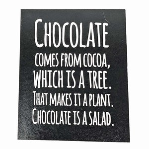 May include: Black and white sign with the text "CHOCOLATE COMES FROM COCOA, WHICH IS A TREE. THAT MAKES IT A PLANT. CHOCOLATE IS A SALAD."