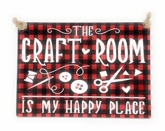 May include: Red and black checkered sign with white text that reads "The Craft Room is My Happy Place". The sign has images of a needle and thread, buttons, and scissors.