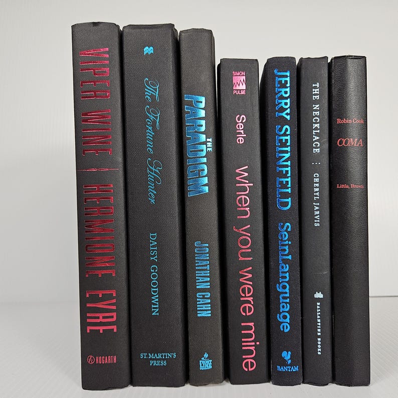 May include: A collection of seven hardcover books with black covers. Titles include "Viper Wine", "The Fortune Hunter", "Paradigm", "When You Were Mine", "Jerry Seinfeld SeinLanguage", "The Necklace", and "Coma". The titles and author names are in various colors.