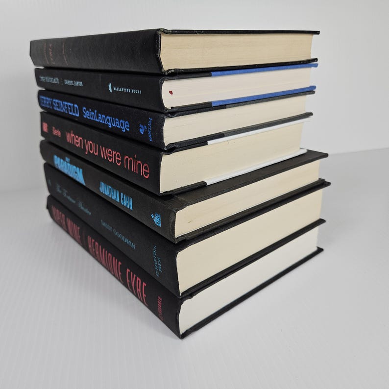May include: A stack of hardcover books with black covers and off-white pages. Titles include "The Untethered Soul", "SeinLanguage", and "When You Were Mine". The books are arranged in a neat pile, with the spines facing the viewer.