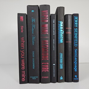 May include: A collection of seven hardcover books with black covers. Titles include "When You Were Mine," "The Fortune Hunter," "Viper Wine," "The Necklace," "The Paradigm," "Coma," and "SeinLanguage." The titles and authors are in various colors.