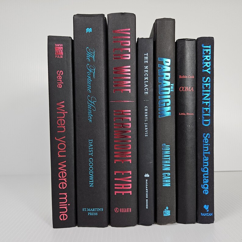 May include: A collection of seven hardcover books with black covers. Titles include "When You Were Mine," "The Fortune Hunter," "Viper Wine," "The Necklace," "The Paradigm," "Coma," and "SeinLanguage." The titles and authors are in various colors.