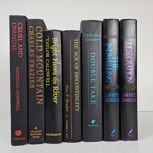 May include: A collection of seven hardcover books with black covers. Titles include "Cruel and Unusual," "Cold Mountain," and "Double Take." The spines feature titles in various colors, including red, gold, and blue.