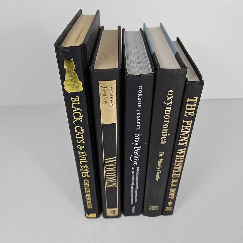 May include: A collection of five hardcover books with black covers. The titles include "Black Cats & Evil Eyes", "Wooden", "Stay Positive", "oxymoronica", and "The Penny Whistle". The books have gold and white lettering.
