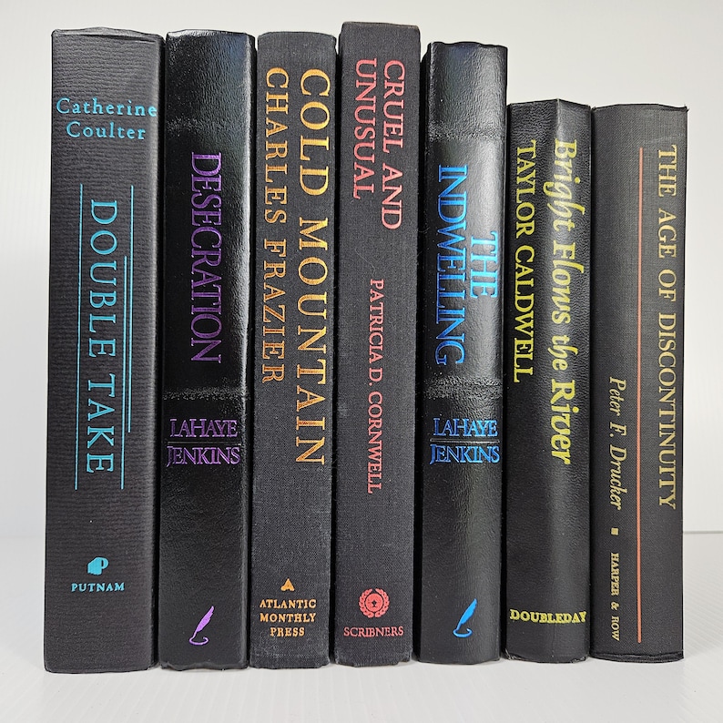 May include: Seven hardcover books with black covers are displayed. Titles include "Double Take," "Desecration," "Cold Mountain," "Cruel and Unusual," "The Indwelling," "Bright Flows the River," and "The Age of Discontinuity." The spines feature author names and publisher imprints.