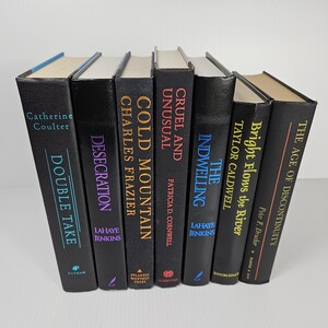 May include: A collection of seven hardcover books with black covers. Titles include "Double Take," "Desecration," "Cold Mountain," "Cruel and Unusual," "The Indwelling," "Bright Flows the River," and "The Age of Discontinuity."