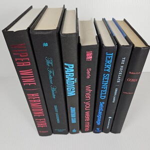 May include: A collection of hardcover books with black covers. Titles include "Viper Wine," "The Fortune Hunter," "The Paradigm," "When You Were Mine," "Jerry Seinfeld," "The Necklace," and "Coma."