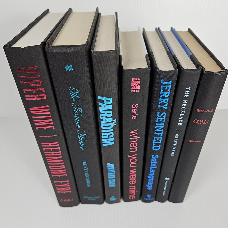 May include: A collection of hardcover books with black covers. Titles include "Viper Wine," "The Fortune Hunter," "The Paradigm," "When You Were Mine," "Jerry Seinfeld," "The Necklace," and "Coma."