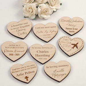 May include: Eight heart-shaped wooden plaques featuring laser-engraved memorial text and names. Each piece displays unique inscriptions such as 'A beautiful soul is never forgotten', dates, and symbols like an airplane or a cross, arranged on a surface.