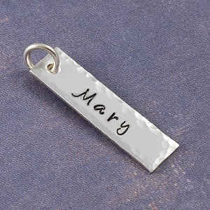 May include: Silver charm with a hammered finish and the name "Mary" engraved on it.