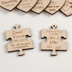 May include: Two wooden puzzle pieces with engraved text. The top piece reads "Rebecca Kennard 1950-2021 You will always be our missing piece". The bottom piece reads "A piece of me is in heaven Arlie A Pelton 1964-2020".