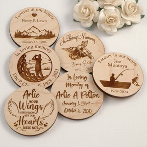 May include: Six wooden memorial coasters with engraved text and images. The coasters feature a heart, mountains, a golfer, a motorcycle, a fisherman, and a pair of angel wings. The text on the coasters includes names, dates, and phrases like "Forever in our hearts" and "In loving memory".