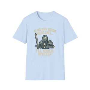 May include: Light blue t-shirt with a humorous graphic of a knight holding a sword. The text reads "IF NO ONE NEEDS HEALING... I'LL TOUCH MYSELF" in a playful font. The knight is depicted in gray and black armor.